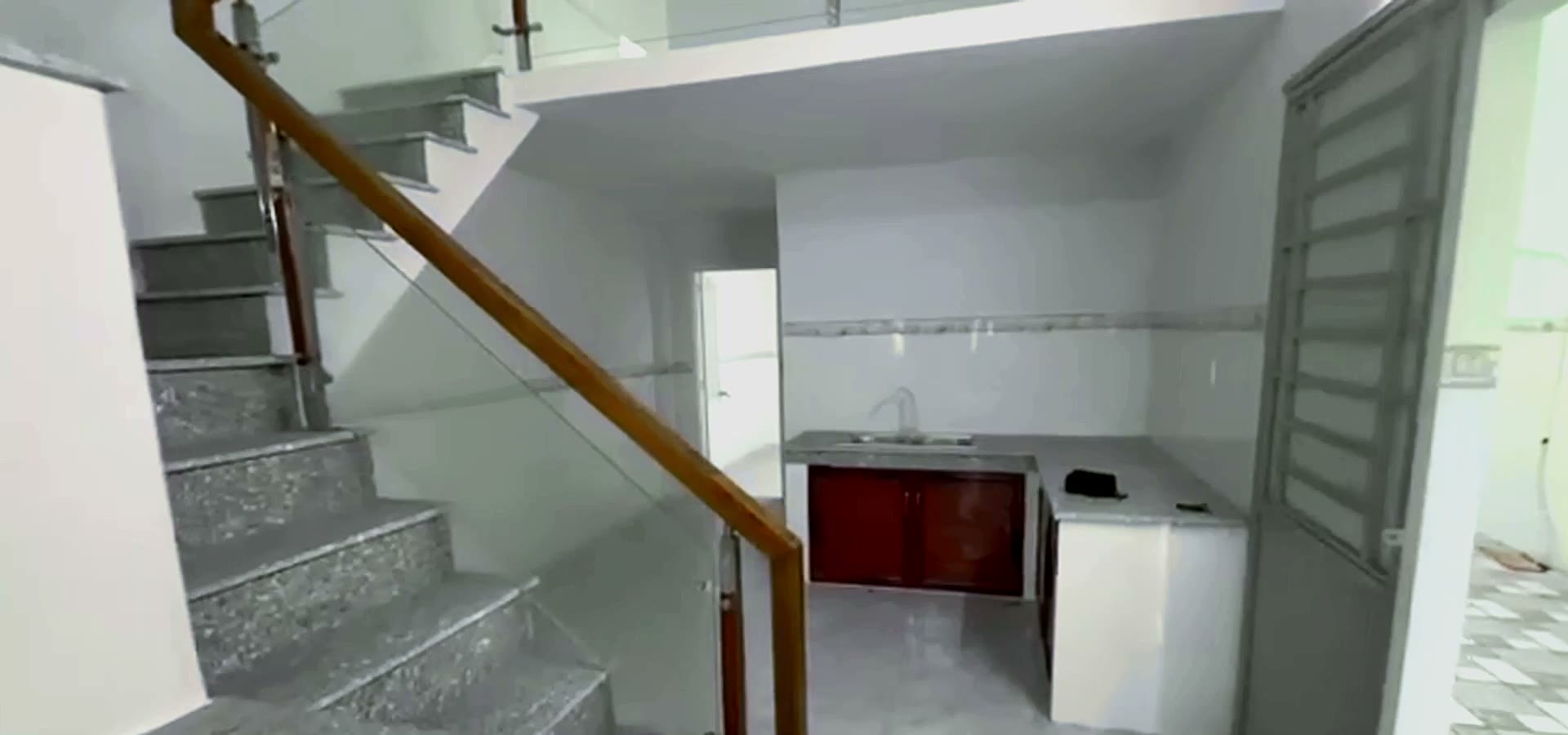 Cầu thang tay vịn gỗ đi ngang ngăn giữa phòng khách và bếp trong nhà gác lửng 3 phòng ngủ ở Mỹ Phước 3