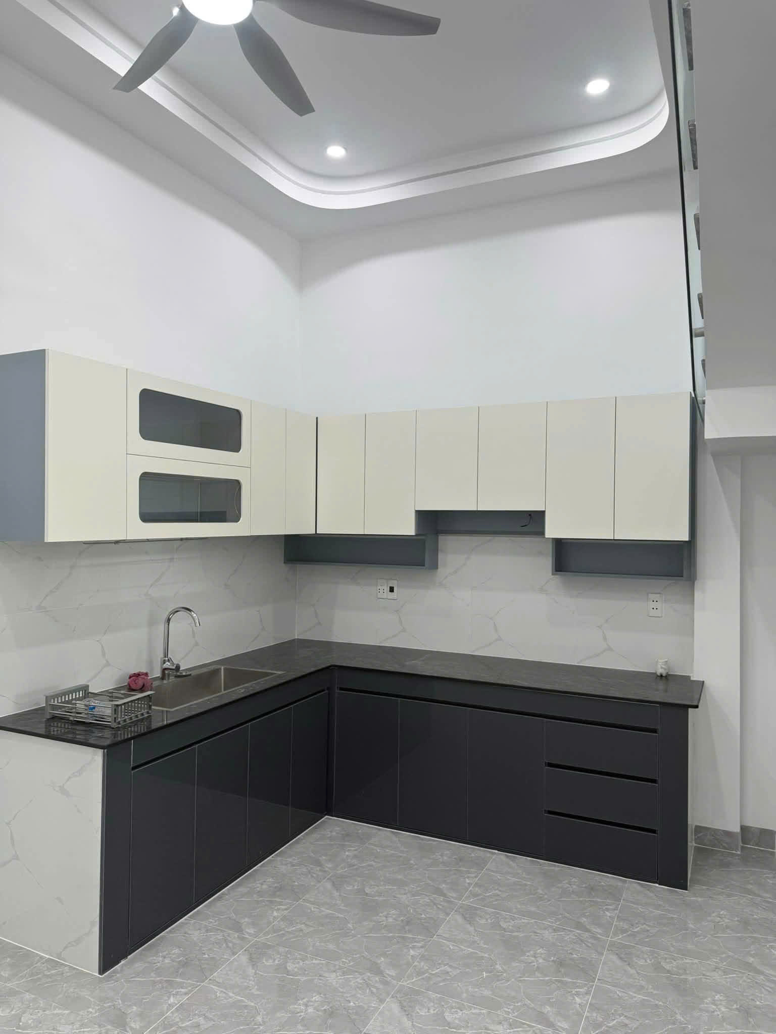 Bếp chữ L tủ trên màu trắng, tủ dưới màu xám trong nhà trục chính ở Bến Cát