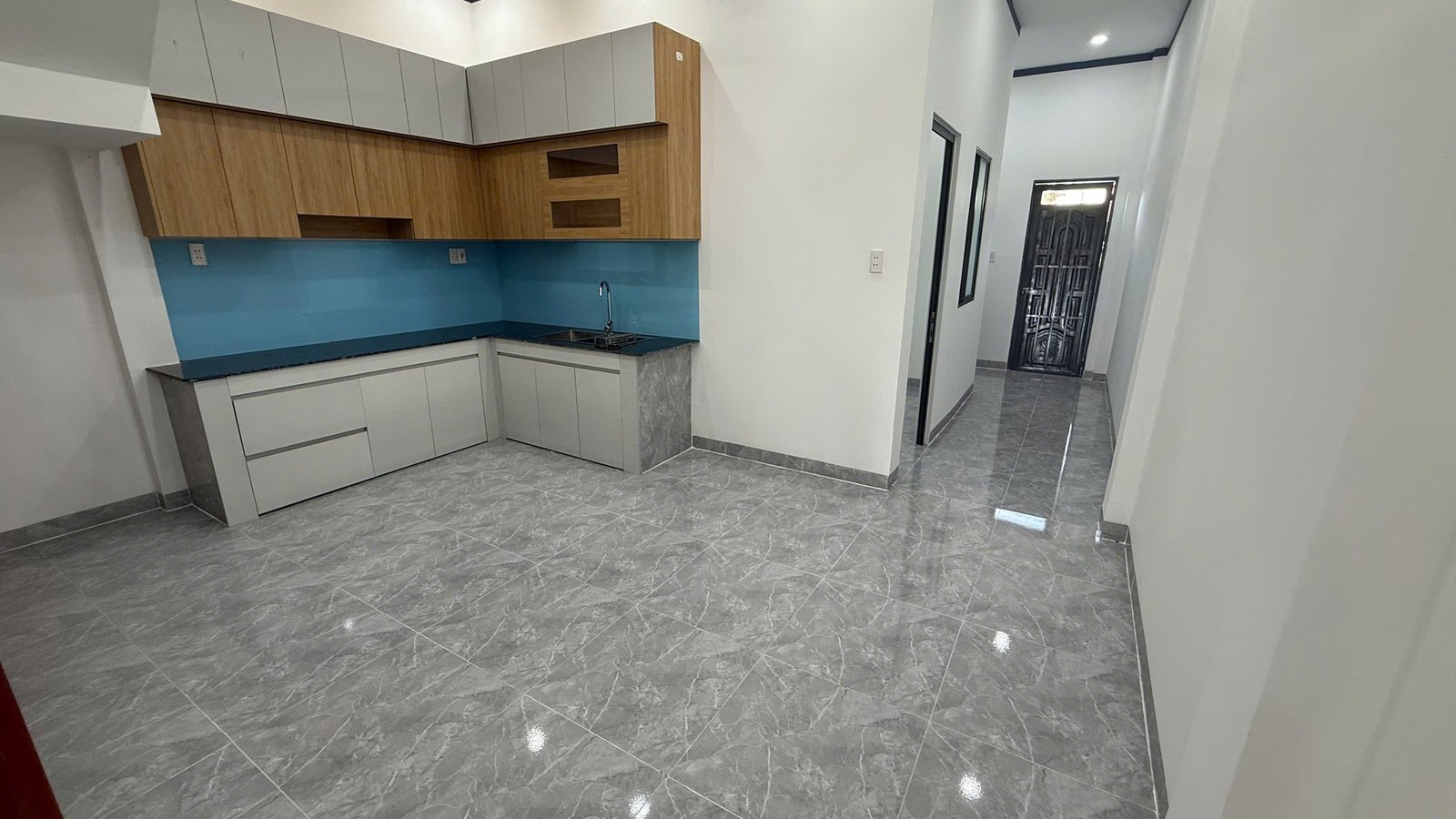 Bếp tầng trệt có tủ bếp trên và tủ bếp dưới, kính ốp xanh, nền gạch xám