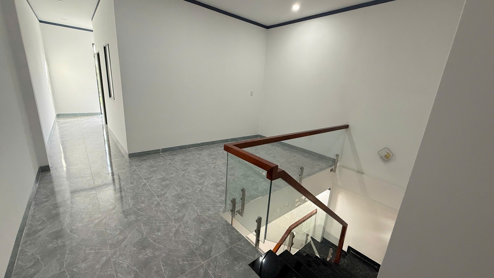Sảnh tầng lầu làm phòng sinh hoạt chung, cạnh cầu thang tay vịn gỗ và kính cường lực